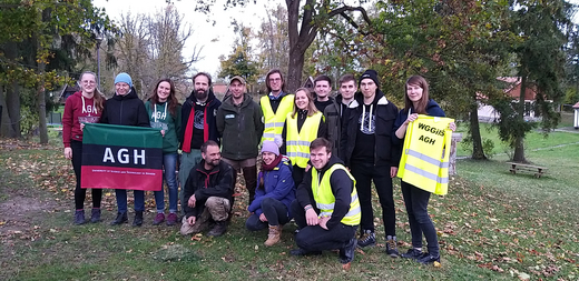 The photo shows a group of young people. One of them is holding a flag with the inscription that says: AGH. Some people wear high-vis vests.
