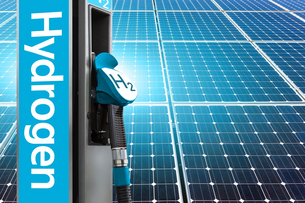 The foreground of the picture features a hydrogen dispenser with a blue inscription hydrogen. The background shows solar panels reflecting sunlight.