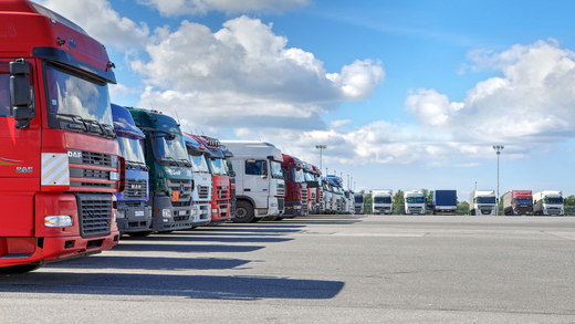 W Polsce największy problem mają firmy, które działają w obszarze transportu czy przetwórstwa przemysłoweg Fotografia przedstawia duży plac, na którym wzdłuż lewego boku i horyzontu stoją zaparkowane w rząd tiry. Środek placu jest pusty, a za linią horyzontu widać błękitne niebo, które częściowo pokryte jest białymi chmurami.