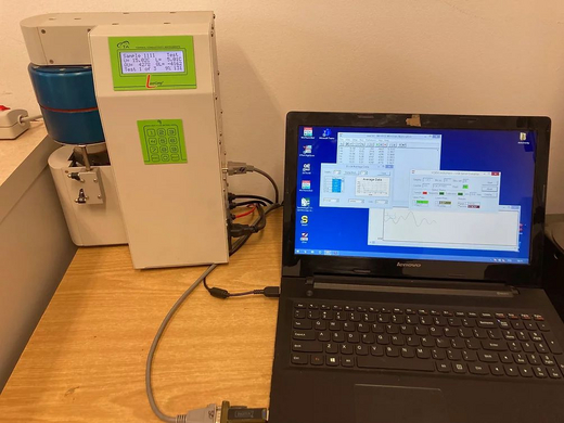 From the left, the photo shows a creamy meter with a green display and a green interface with numerals. To the right is a black laptop that displays various windows that show data in the form of numbers and charts.