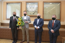 Zdjęcie wykonane w sali konferencyjnej. Na pierwszym planie stoją bok siebie, od lewej: Rektor AGH prof. Jerzy Lis, laureat Tomasz Kraus, prezes Fundacji dla AGH dr inż. Jerzy Kicki, prezes Stowarzyszenia Wychowanków AGH prof. Piotr Czaja. Usta i nosy stoj