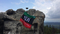 On the left side, there is a GNSS receiver. It is the colour of steel and stands on a tripod. The AGH UST flag is wrapped around the tripod. The flag is composed of three horizontal stripes coloured, from the top, green, black, and red. The background of the photo constitutes a mountain crest. Granite rocks covered in green flora are visible. Above the mountain crest there is a blue sky, which is partly covered by white and grey clouds.