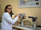 The photo shows a young woman in a lab coat standing in front of a silver high-temperature microscope.