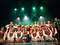 Na scenie widoczna w dwóch rzędach grupa dzieci w strojach krakowskich. W pierwszym rzędzie, widoczna dziewczynka trzymająca dyplom z napisem Grand Prix. Przyciemniona sala - nad dziećmi widoczne reflektory świecące na zielono.