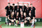 The photo shows the AGH UST team of floorball players after the presentation of medals. There are six men standing in a row and below, there are five women squatting. All are wearing the same clothes: black T-shirts, black  shorts, sports shoes. They all have medals hanging around their necks. In front of the players, there is a cup and a diploma. The photo was taken in a sports hall.